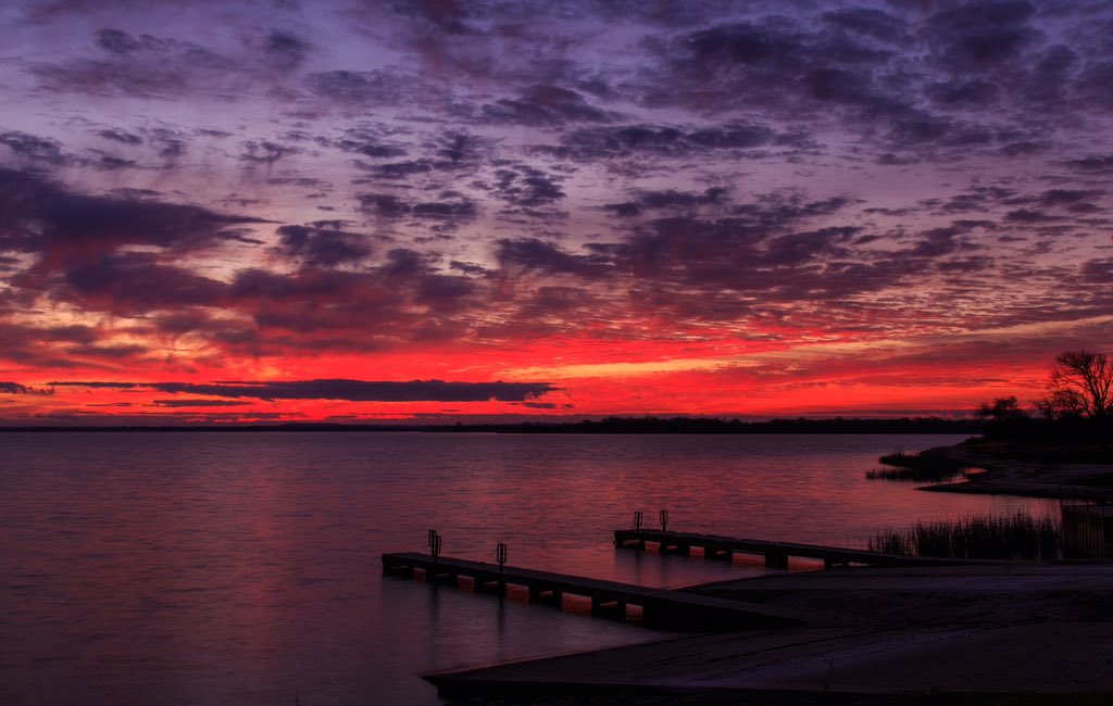 Lake Somerville at sunset with crimson and violet sky reflected on the water and a wooden dock